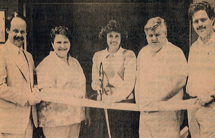 A newspaper clipping of Robert Gill and family, cutting the ribbon outside their new location in the early 1980s